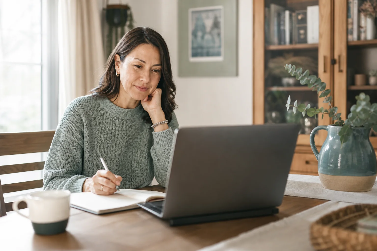 A parent participating in a private consultation from home, listening thoughtfully with notes nearby