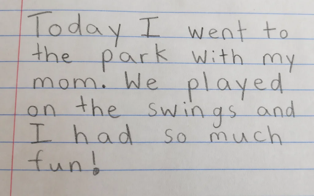 Close view of a child's messy handwriting on lined paper with a pencil